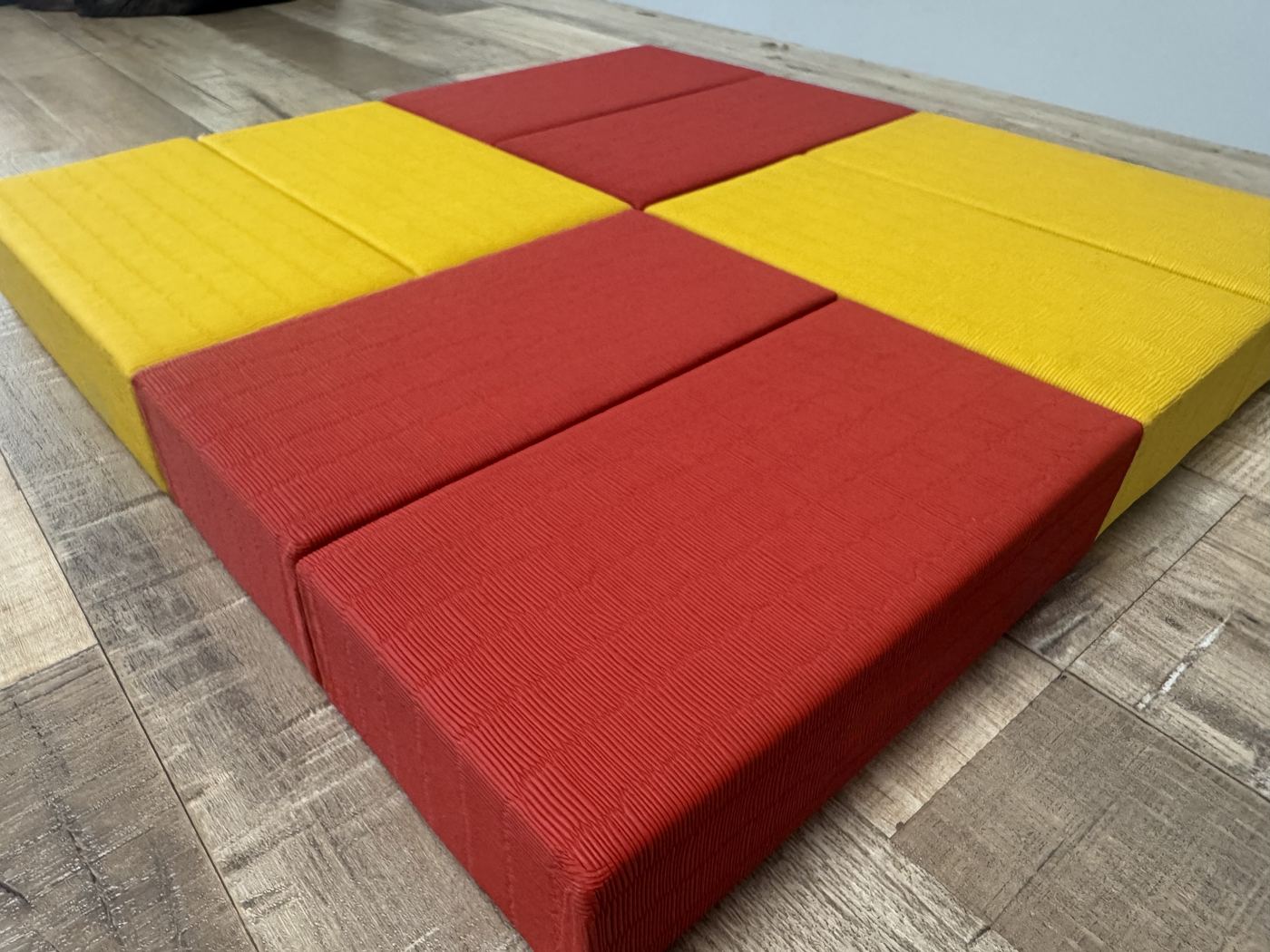 Judo tatami tiles in alternating red and yellow laid edge to edge on a floor — close view of the fine surface grain and tile thickness