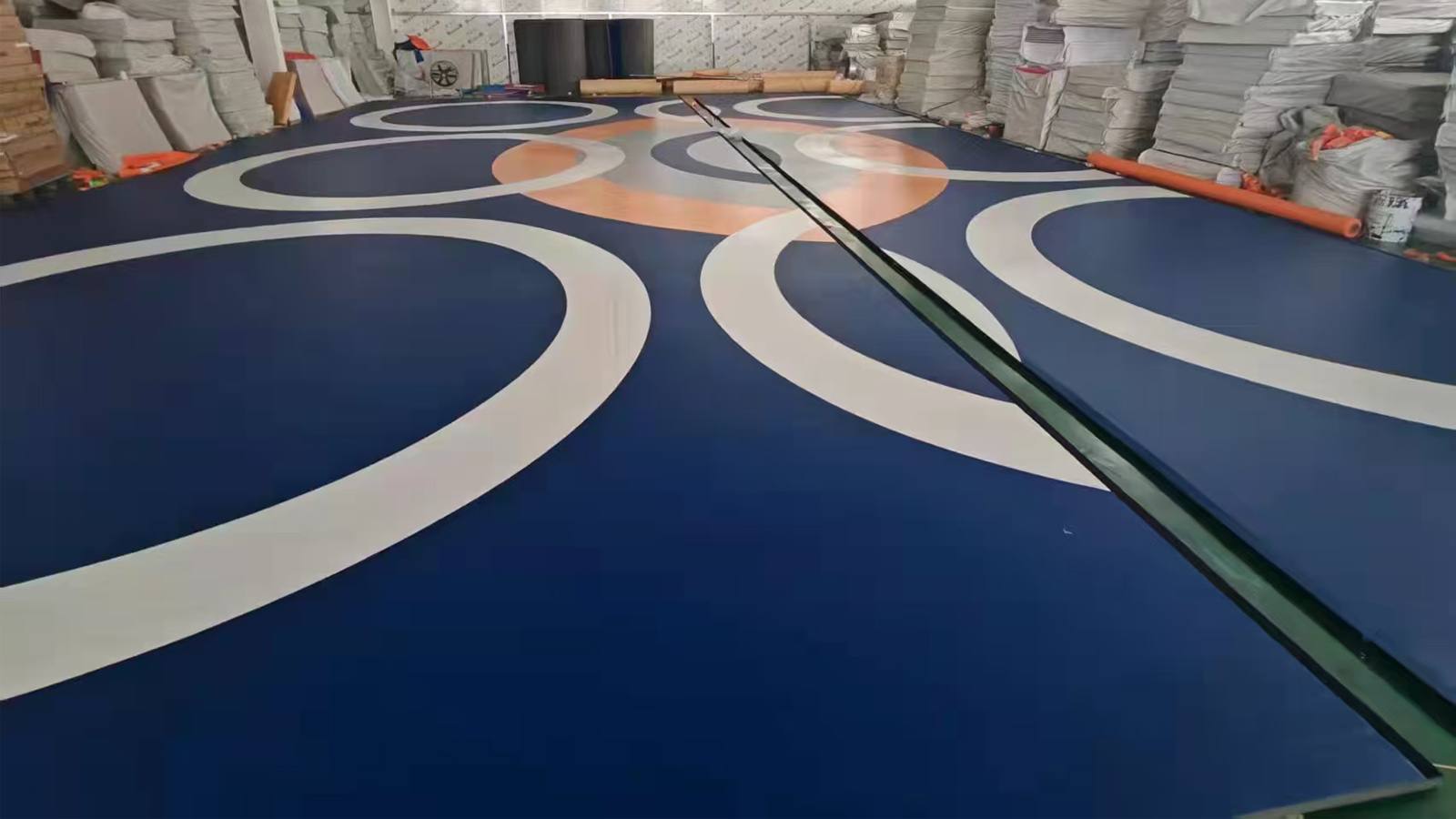 Wrestling mat surface with blue, orange and white ring graphics laid out in the factory bay